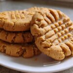A close-up stack of four golden brown peanut butter cookies showing the classic crosshatch fork marks on top.