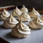 Close-up of freshly piped, creamy white meringue cookies arranged on parchment paper.