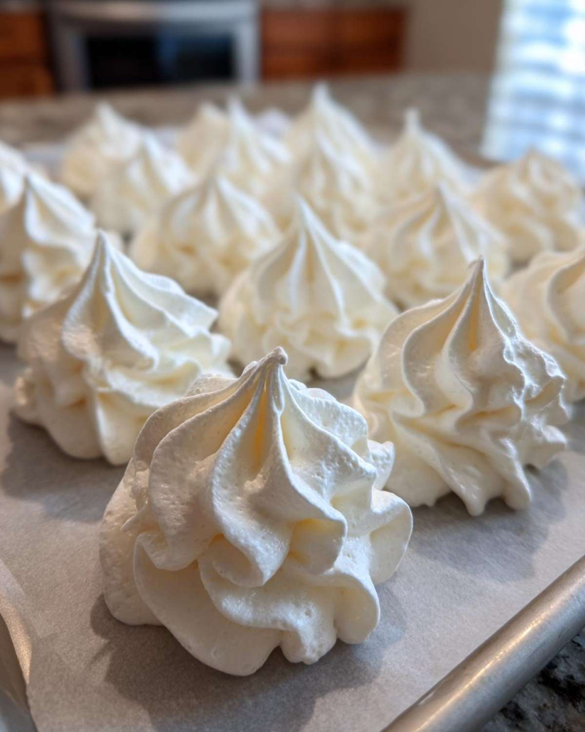 Close-up of several perfectly piped, white meringue cookies sitting on parchment paper on a baking sheet.