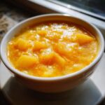 Close-up of a hearty bowl of bright orange potato cheese soup, garnished with paprika.