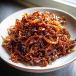 Close-up of a small white bowl filled with deeply browned, glossy caramelized onions.