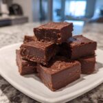 A stack of rich, dark chocolate fudge squares piled high on a small white plate.