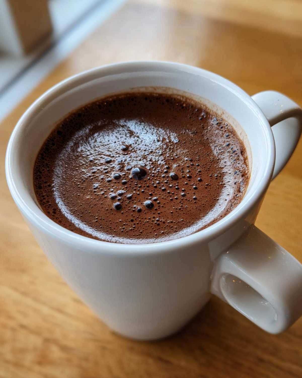 Close-up of rich, dark brown hot cocoa mix topped with small bubbles in a white ceramic mug.