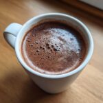 Close-up of a white mug filled with rich, dark hot cocoa mix, showing a layer of small bubbles on top.