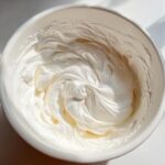 Close-up overhead shot of thick, glossy white royal icing recipe mixture swirled in a white mixing bowl.