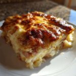 A close-up of a square serving of creamy scalloped potatoes and ham with a deeply browned, cheesy crust.