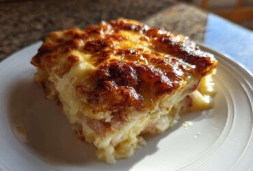 A close-up of a square serving of creamy scalloped potatoes and ham with a deeply browned, cheesy crust.