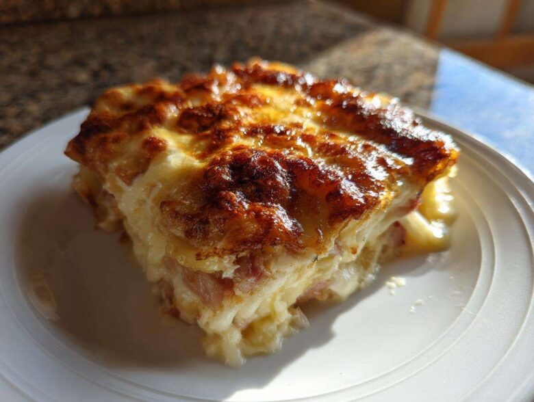 A close-up of a square serving of creamy scalloped potatoes and ham with a deeply browned, cheesy crust.