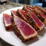 Slices of perfectly cooked Seared Ahi Tuna, crusted with black and white sesame seeds, showing a bright pink center.