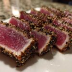 Close-up of perfectly seared ahi tuna, sliced to show the rare, deep red center and sesame seed crust.