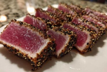 Close-up of perfectly seared ahi tuna, sliced to show the rare, deep red center and sesame seed crust.