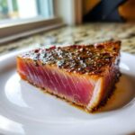 Close-up of a thick, perfectly seared tuna steak showing a deep pink, rare center, coated in a flavorful MARINADE FOR TUNA STEAK.