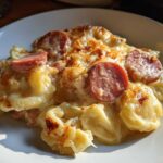 A close-up serving of baked pierogi casserole topped with melted cheese and slices of smoked sausage.
