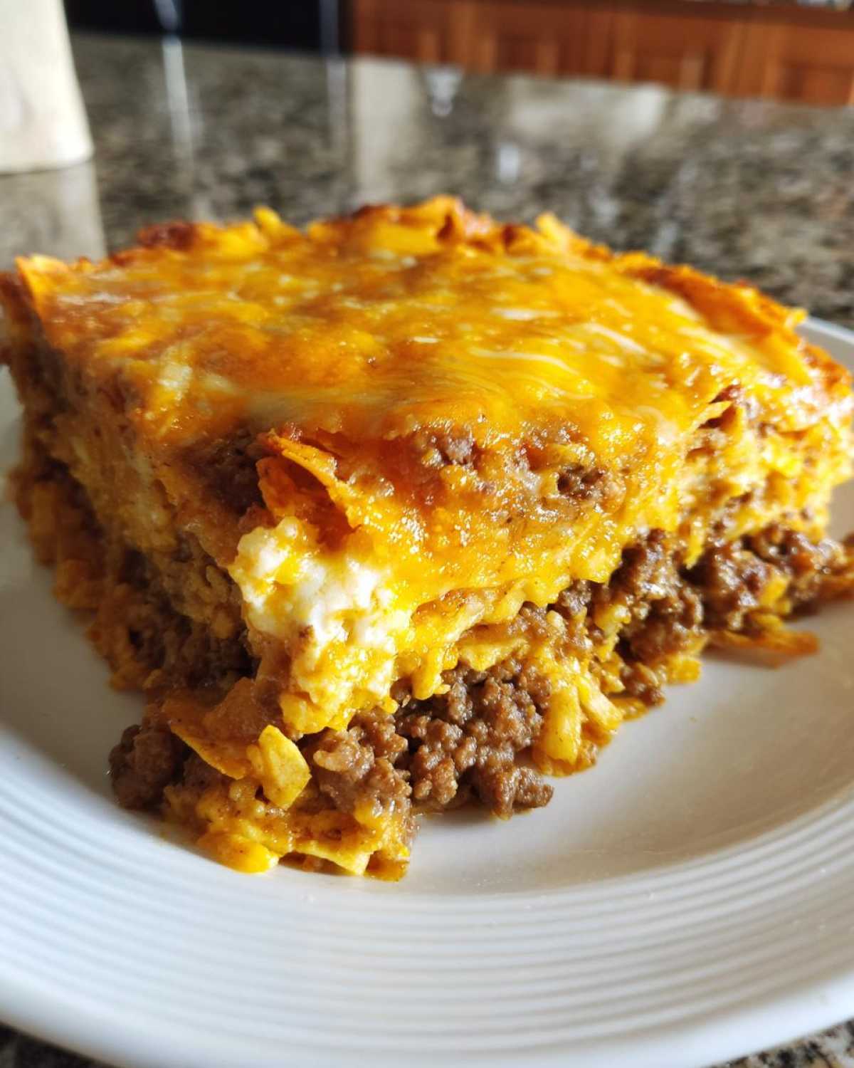 A thick slice of Dorito Casserole showing layers of seasoned ground beef, creamy sauce, and melted cheddar cheese topping.
