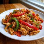 Close-up of shredded chicken mixed with colorful red and green bell peppers for crockpot chicken fajitas.