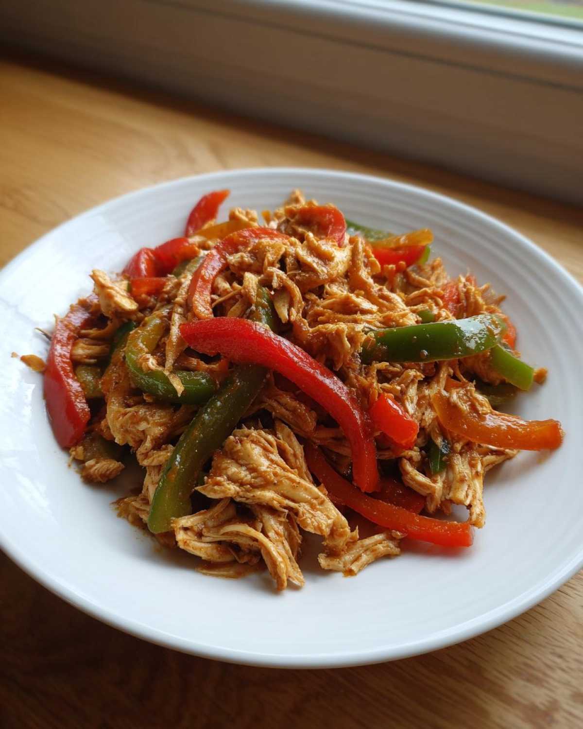 A white plate filled with shredded chicken mixed with sliced red and green bell peppers, ready for crockpot chicken fajitas.