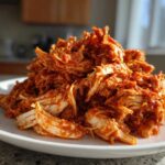 A mound of vibrant, shredded chicken tinga coated in rich red sauce piled high on a white plate.