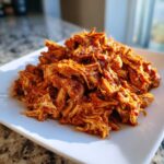 A mound of saucy, shredded chicken tinga piled high on a square white plate.
