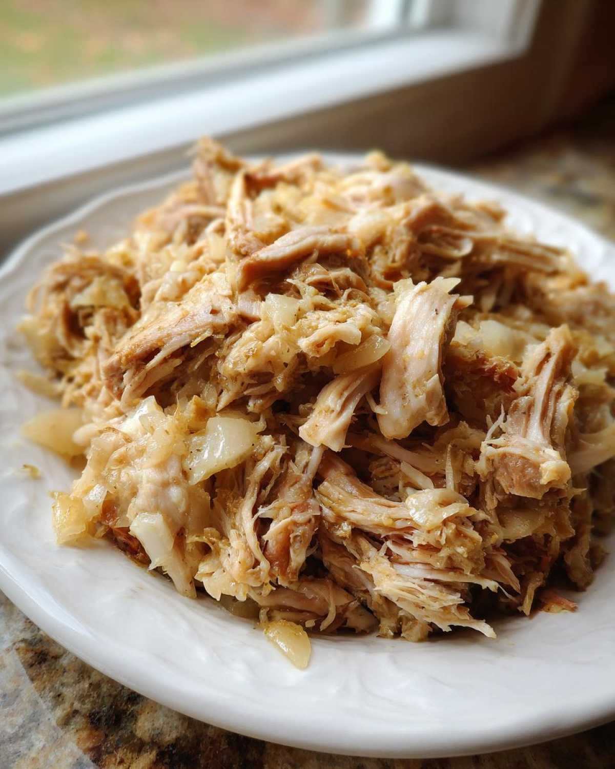 Close-up of tender, shredded pork and sauerkraut mixture served on a white plate.