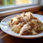 A serving of tender, shredded pork and sauerkraut mixture on a white plate near a window.