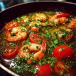 Close-up of pink shrimp and bright red tomato slices simmering in the flavorful broth of tom yum soup, garnished with fresh herbs.