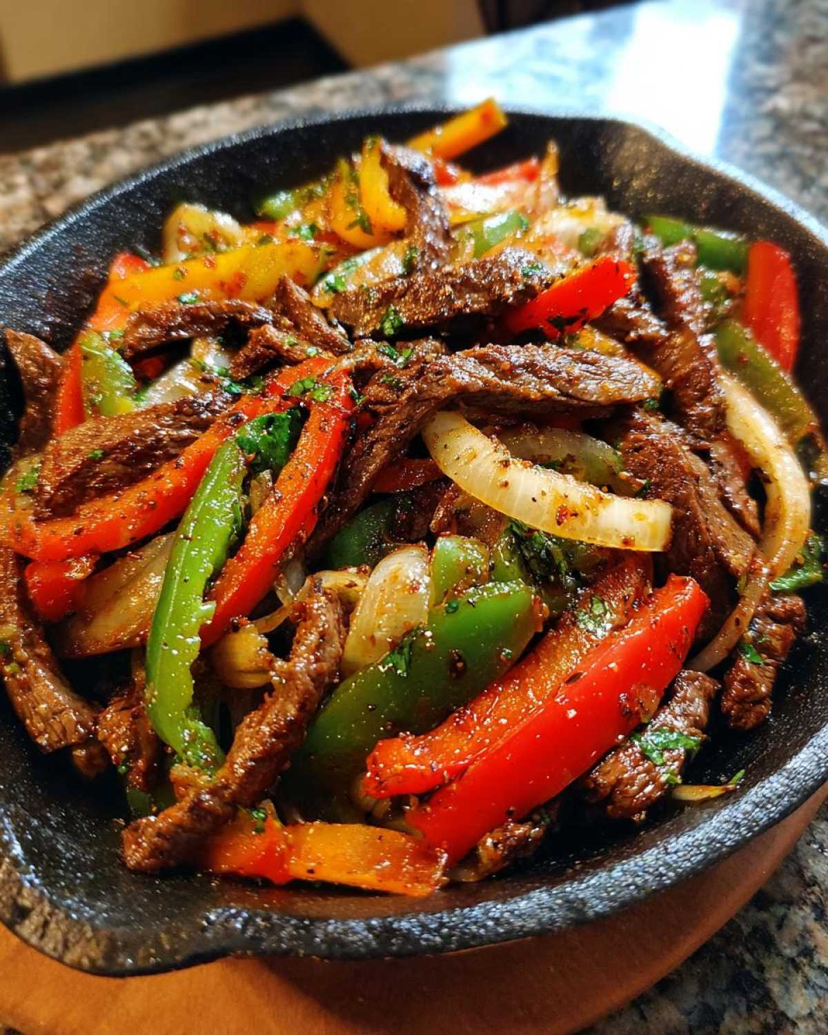 Close-up of sizzling steak fajitas with colorful bell peppers and onions served in a black cast iron skillet.