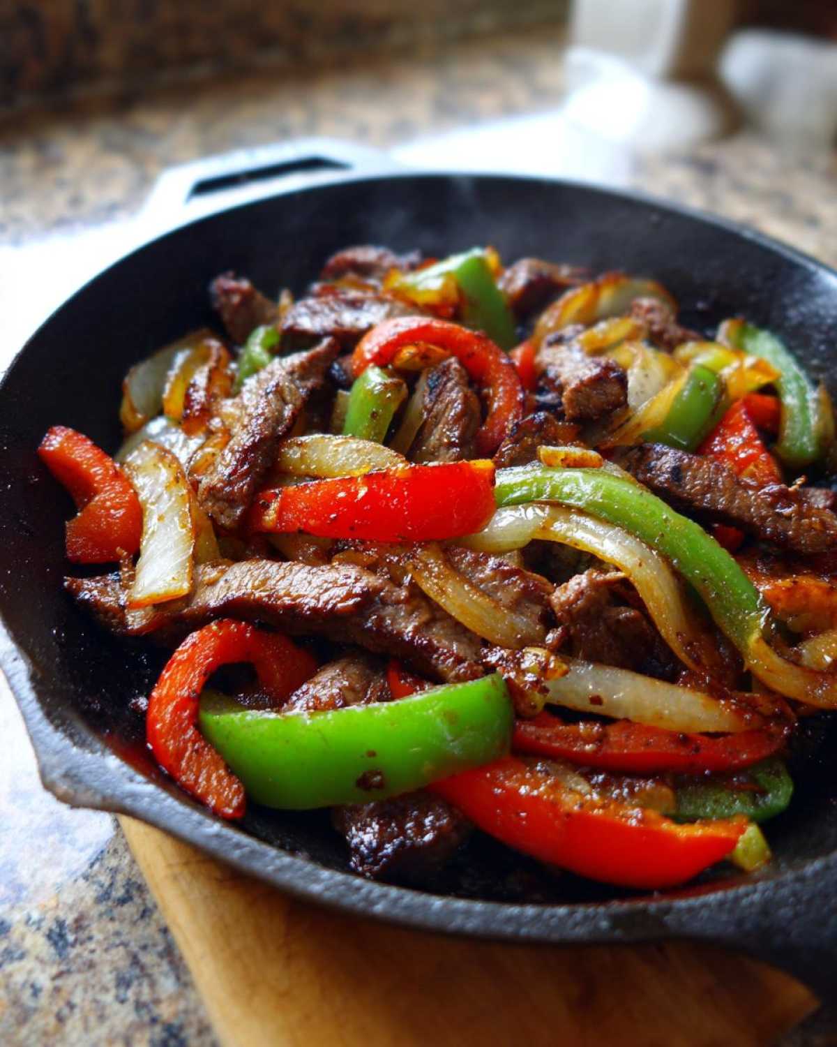 Close-up of sizzling steak fajitas with colorful bell peppers and onions served in a hot cast iron skillet.