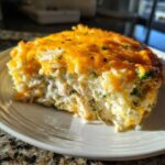 A generous slice of cheesy chicken and rice casserole topped with melted cheddar cheese, served on a white plate.