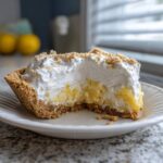 A close-up slice of million dollar pie showing the graham cracker crust, yellow filling, and whipped topping sprinkled with crumbs.