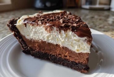 A close-up slice of a 4-layer mud pie showing chocolate crust, mousse, whipped cream, and chocolate shavings.