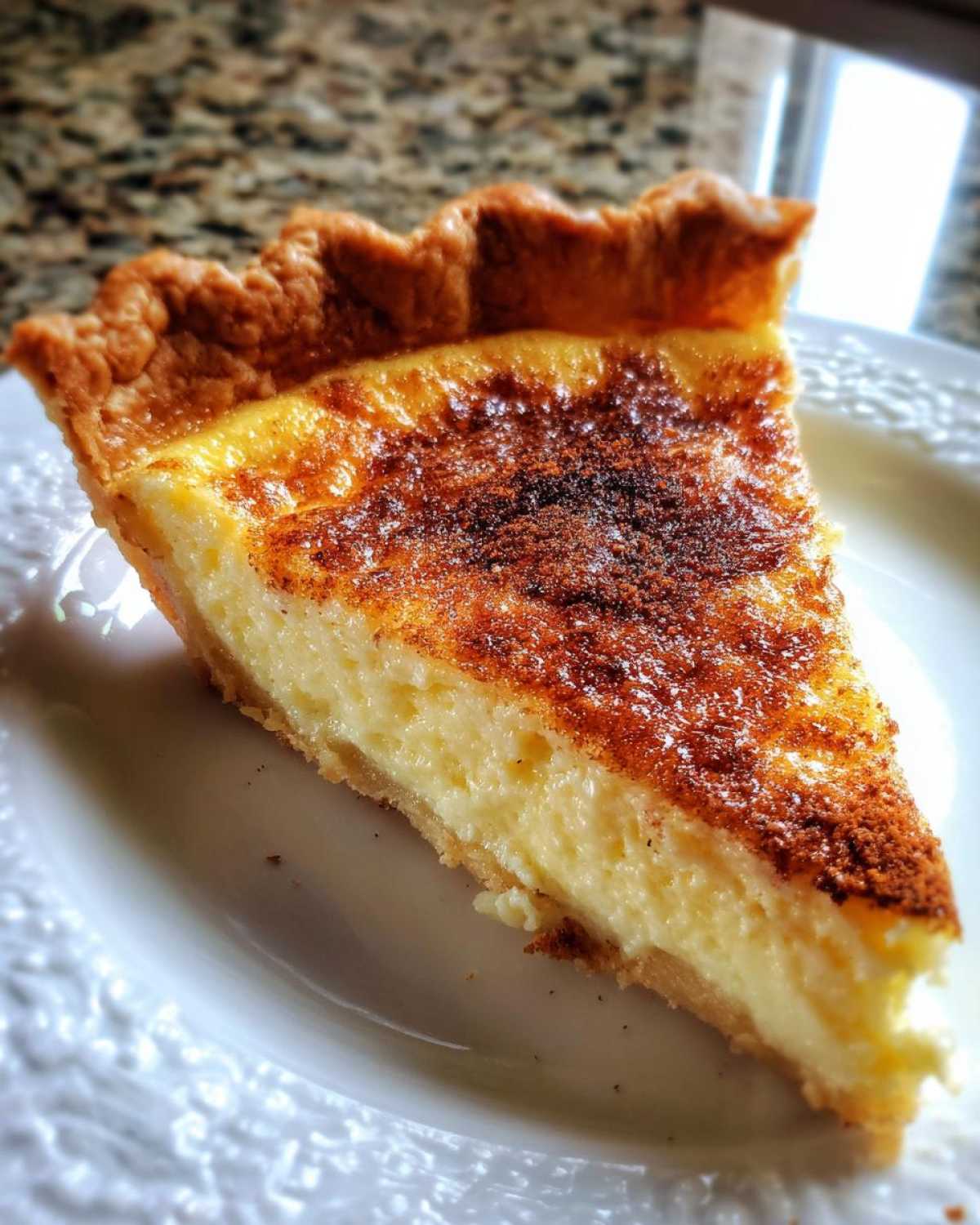 A close-up of a slice of creamy egg custard pie with a golden-brown, spiced top crust.