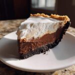 A perfect slice of 4-layer mud pie showing a dark crust, rich chocolate filling, and fluffy white topping.