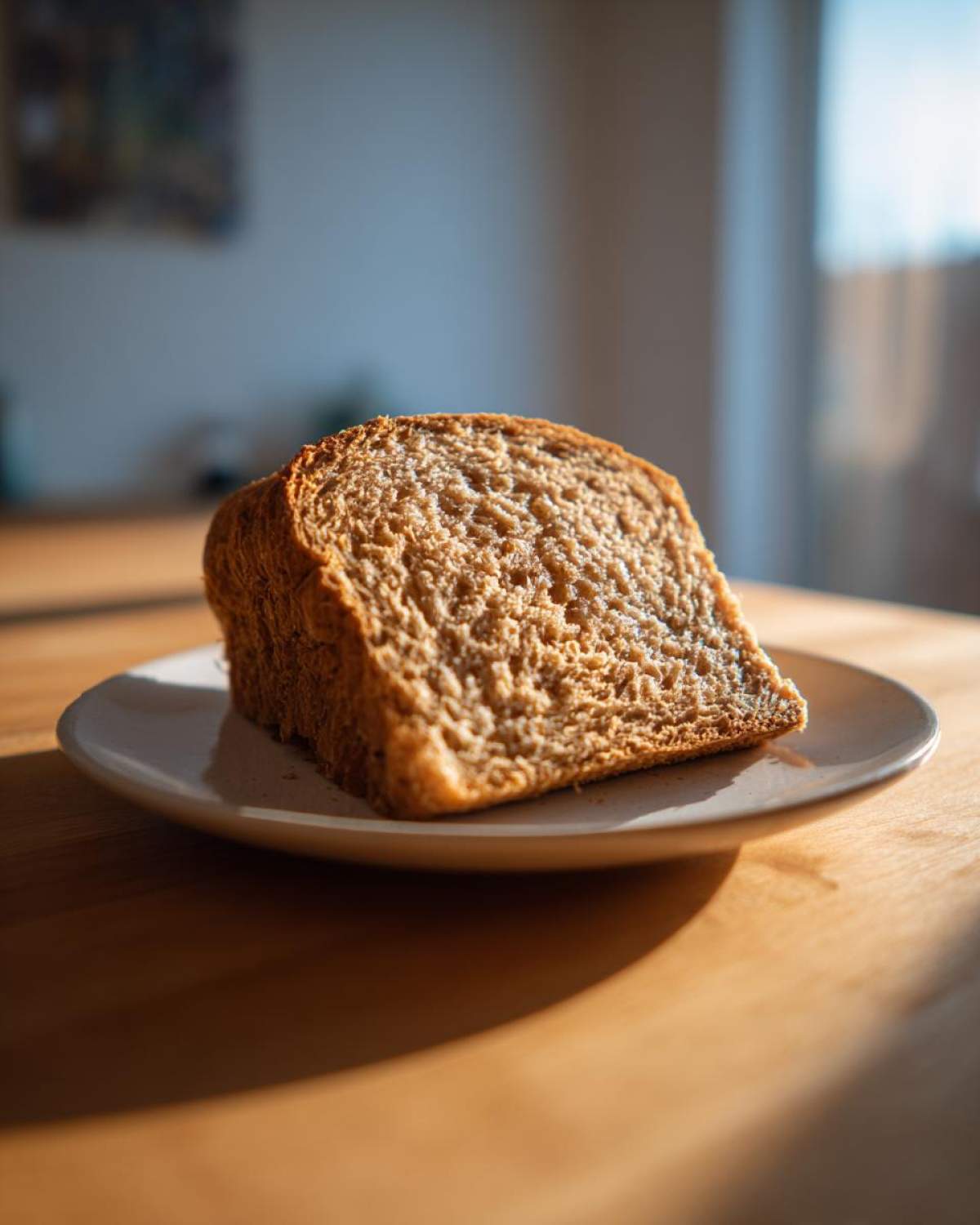 A thick, perfectly baked slice of whole wheat bread resting on a small white plate, illuminated by natural light.
