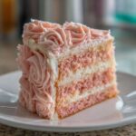 A close-up of a slice of pink layer rose cake featuring alternating pink cake and white filling layers, decorated with pink frosting rosettes.