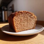 A thick slice of freshly baked whole wheat bread showing its soft, porous crumb, served on a white plate.