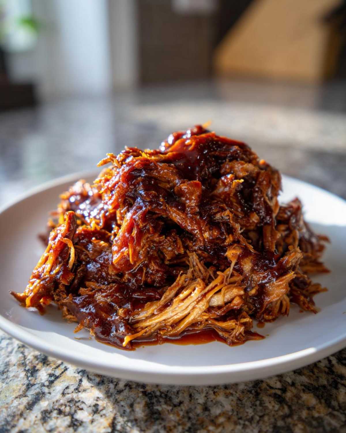 A close-up of tender, saucy Slow cooker pulled pork piled high on a white plate.