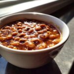 A close-up of rich, saucy black eyed peas served in a white bowl, glistening in natural light.