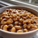 A close-up shot of rich, savory black eyed peas simmering in a flavorful broth inside a white bowl.