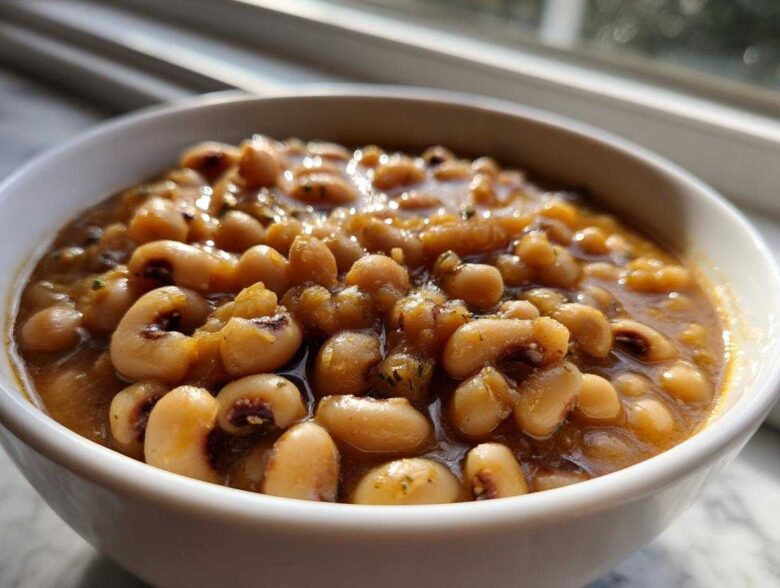 A close-up shot of rich, savory black eyed peas simmering in a flavorful broth inside a white bowl.