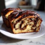 Close-up of a soft chocolate babka loaf, sliced to show the rich, swirled chocolate filling and glossy topping.