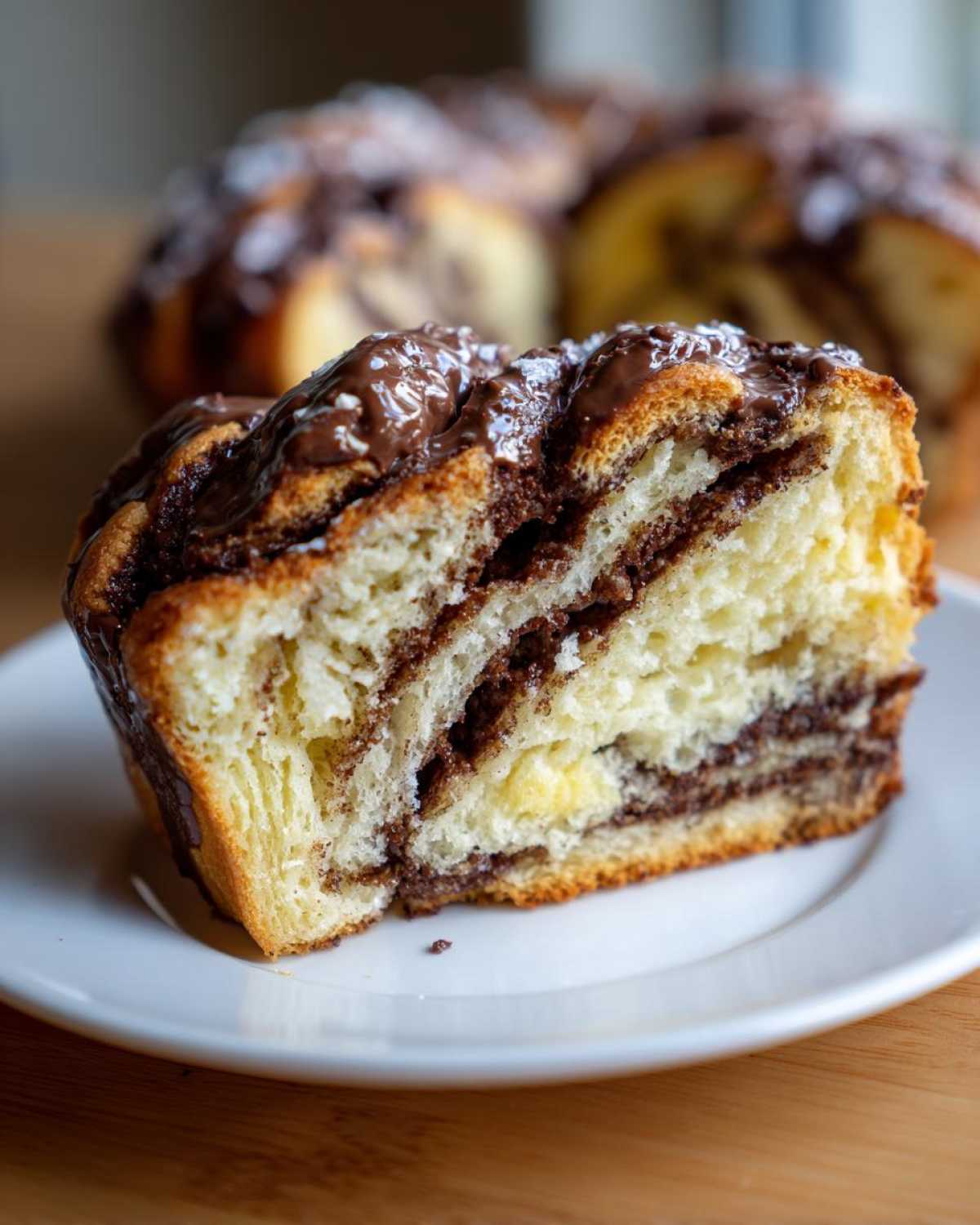 Close-up of a soft slice of chocolate babka showing layers of dough and rich chocolate filling, topped with glaze.