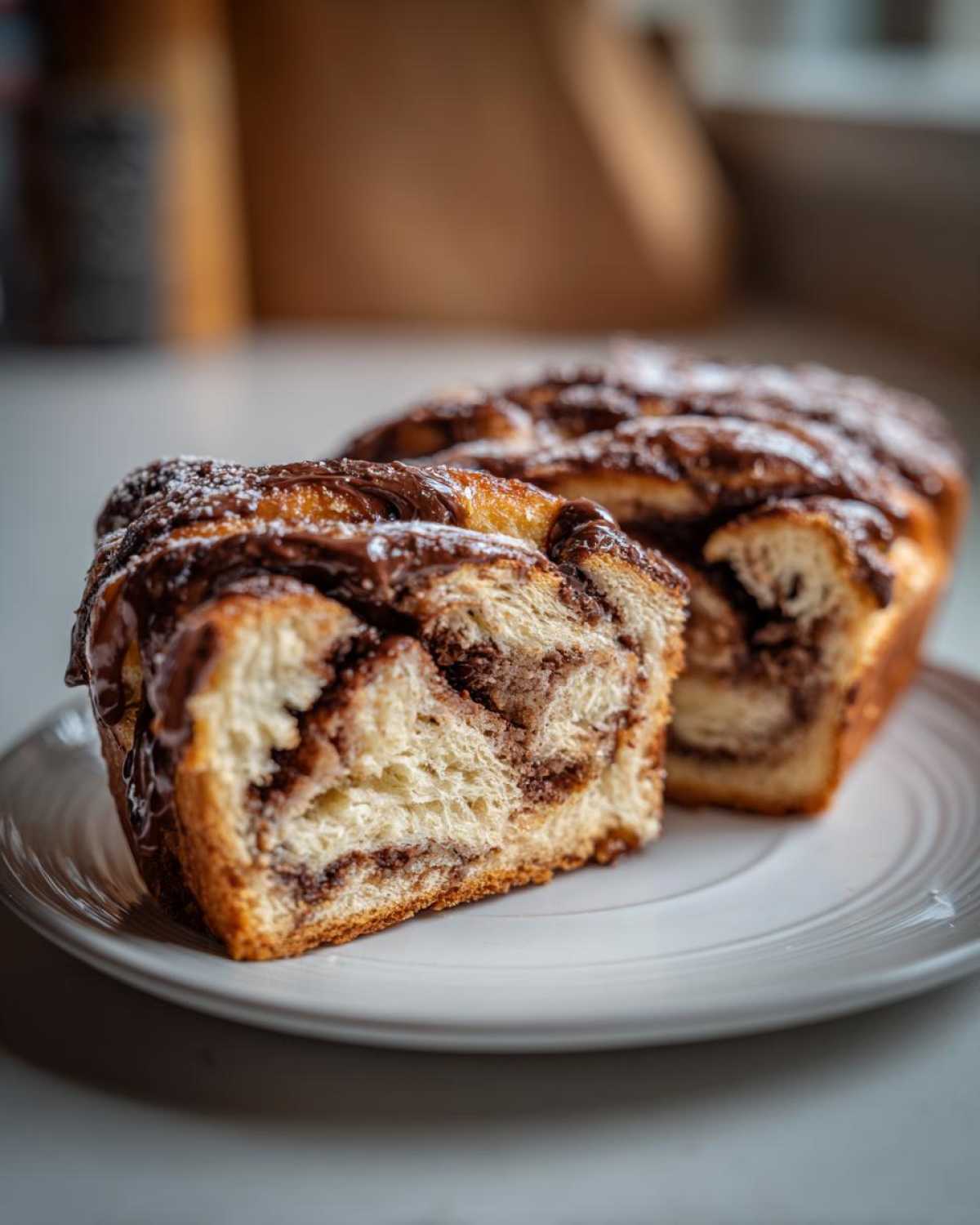 A close-up of a slice of soft chocolate babka showing the swirled filling, topped with chocolate glaze and powdered sugar.
