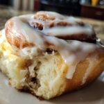 A close-up shot of a soft, fluffy cinnamon roll with a generous swirl of white icing, showing a bite taken out.