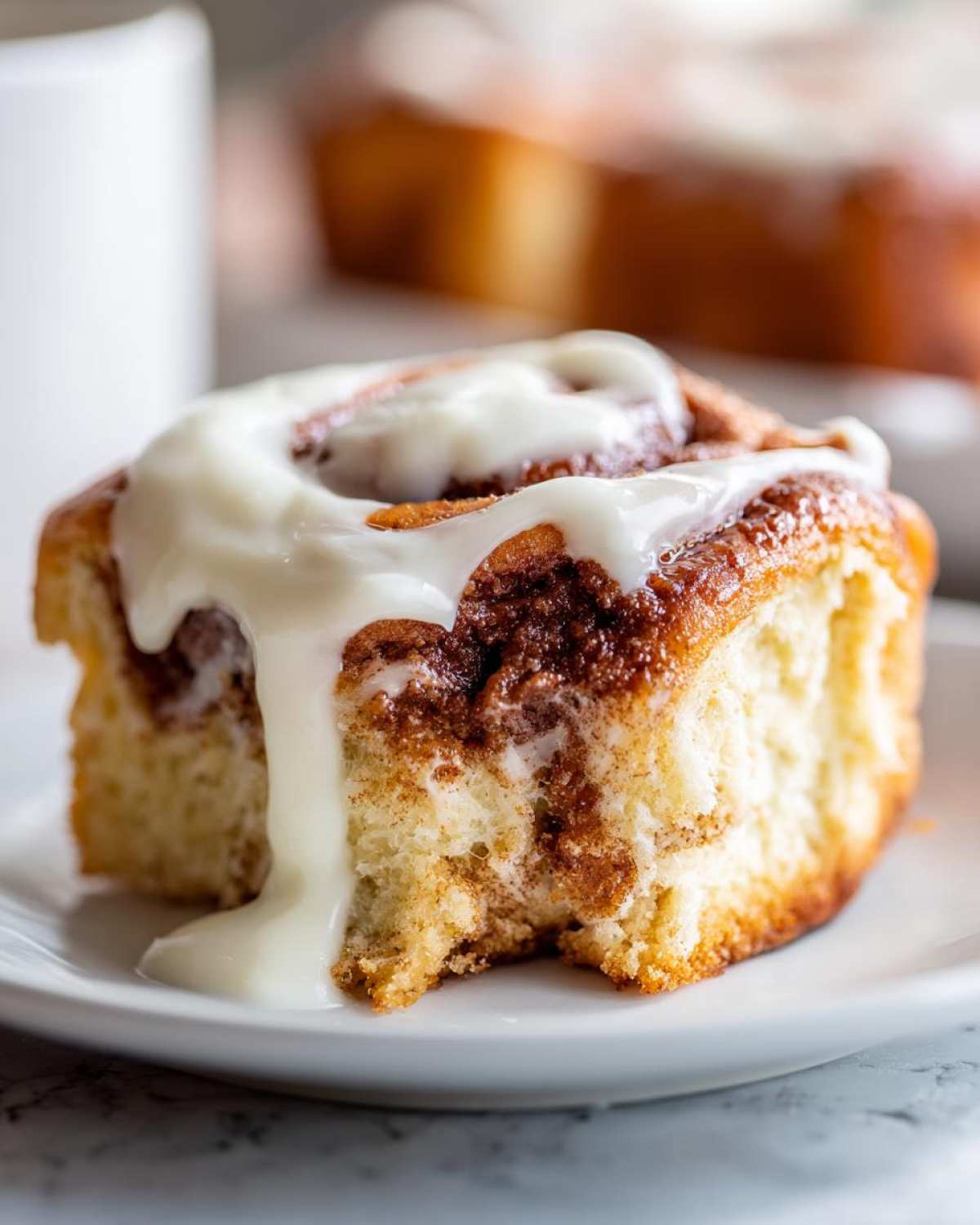 A close-up of a soft, fluffy cinnamon roll generously topped with dripping white cream cheese icing.