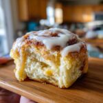 A close-up view of a soft, fluffy cinnamon roll with thick white icing, showing the interior texture.