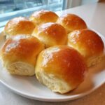 A plate of six golden-brown, shiny dinner rolls fresh from the oven.