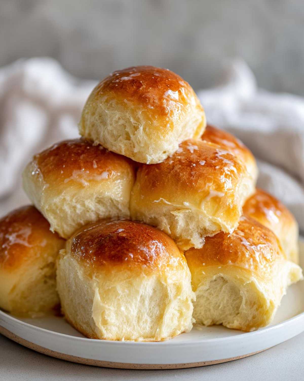 A stack of freshly baked, golden-brown dinner rolls with a light glaze, ready to serve.