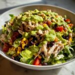 A vibrant bowl of southwest chicken salad topped with shredded chicken, corn, black beans, tomatoes, and creamy green dressing.