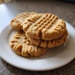 A close-up stack of four tender peanut butter cookies showing classic crosshatch fork marks on a white plate.
