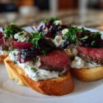 Close-up of three steak crostini appetizers featuring medium-rare steak, creamy cheese spread, and caramelized onions.